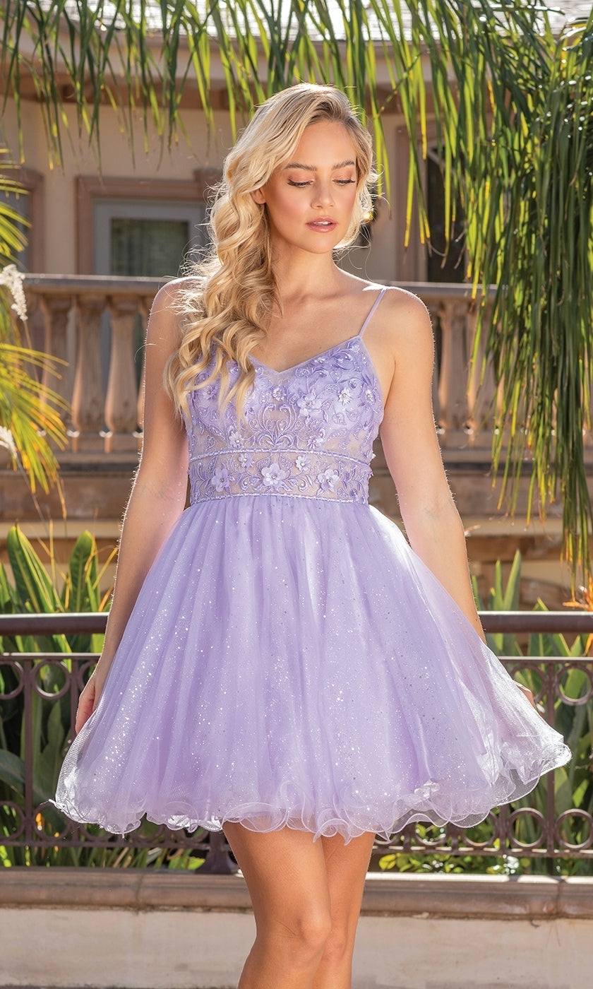 A woman stands outdoors in the Glitter-Tulle Short A-Line Homecoming Dress 3336, featuring light purple tulle, a sleeveless lace bodice with an embellished v-neck, and a short skirt. Lush greenery and a building are visible behind her.